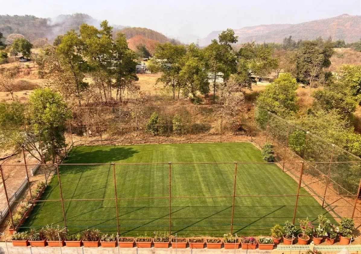 Fenced green cricket turf overlooking the Sahyadri mountains